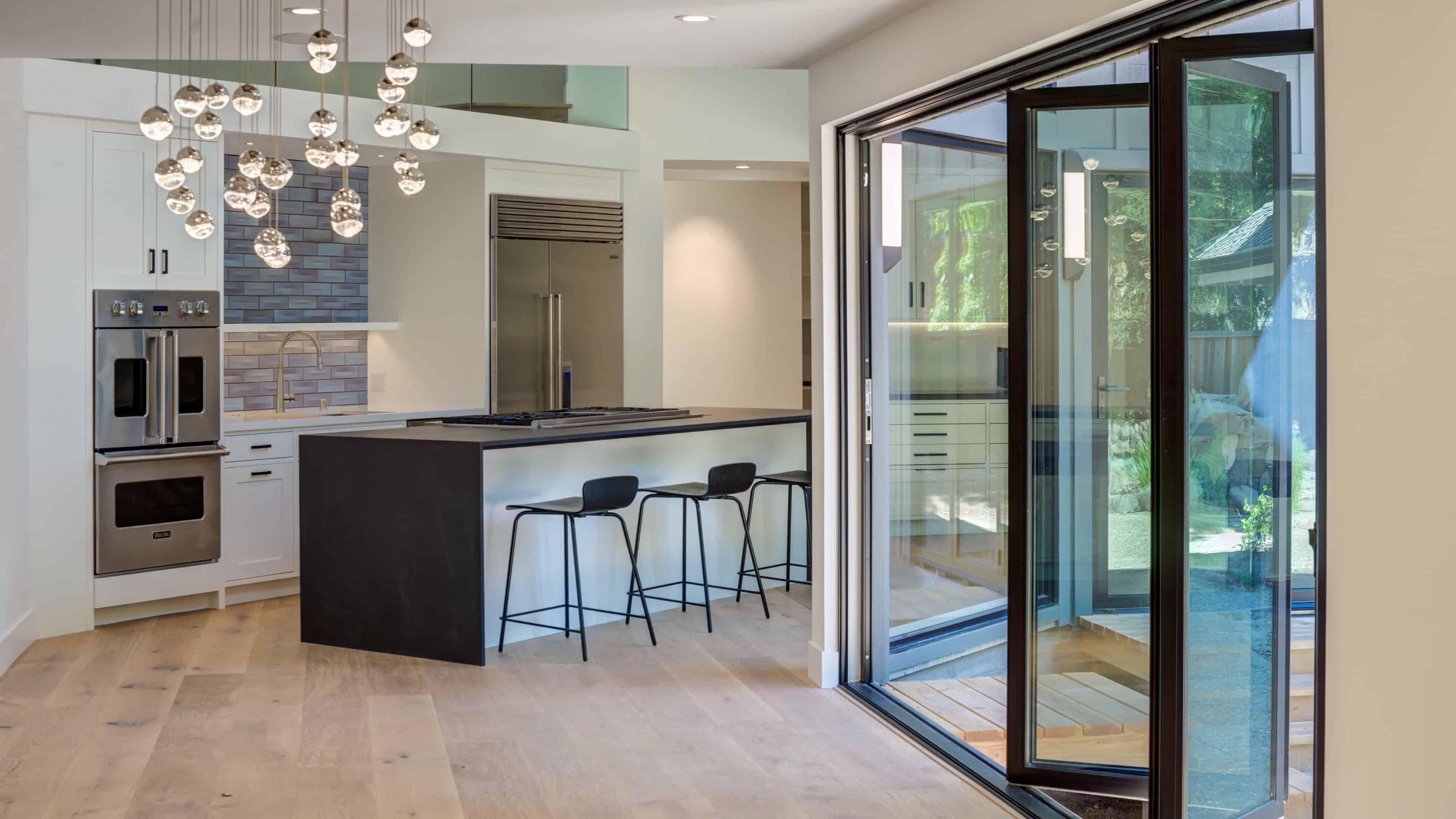 Interior view of sleek modern home with kitchen and large glass doors to the exterior.