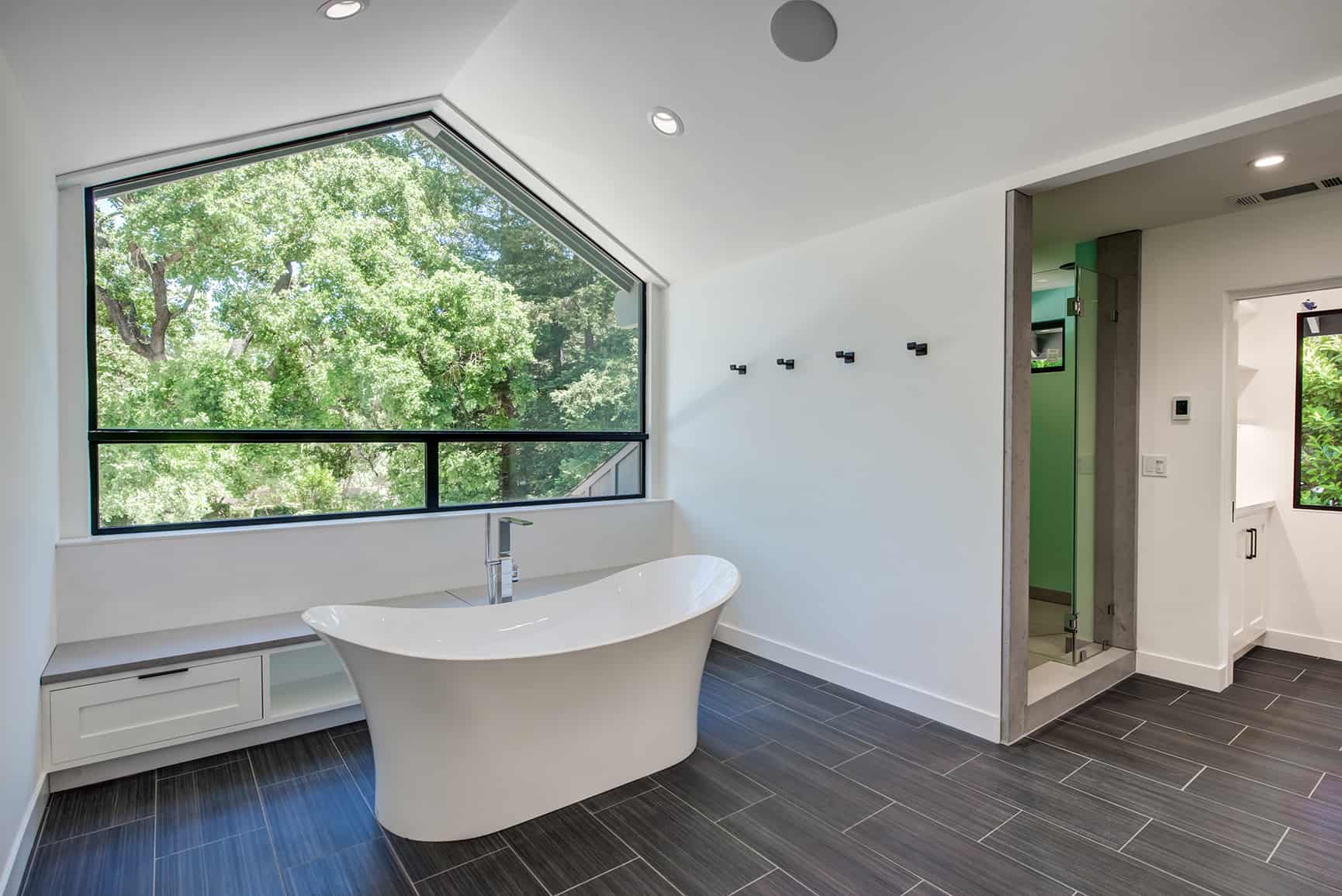 Freestanding bathtub in large master bathroom with view of treetops through large window.