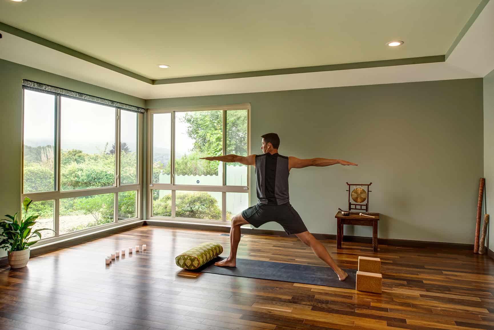 Homeowner practicing yoga in his newly build studio with large glass windows.