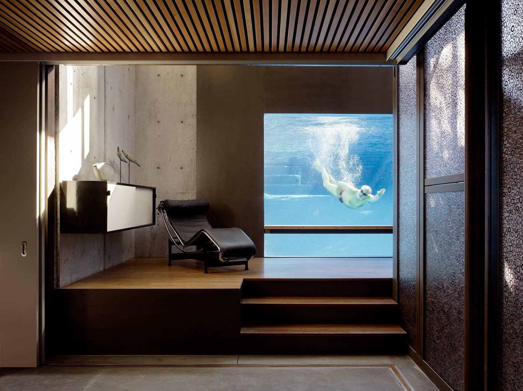 Mid-century modern interior with view of homeowner swimming in pool.