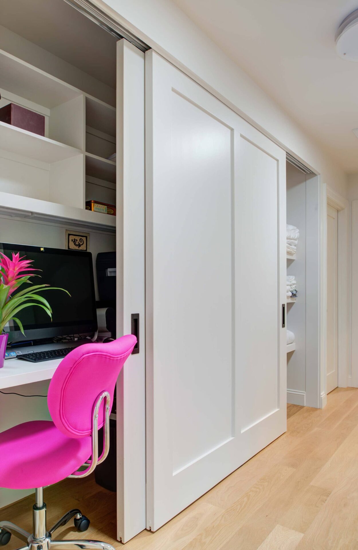 Office space built into closet with pink desk chair.